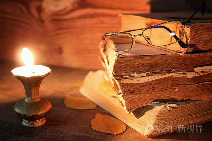 老破破烂烂的书，一张小木桌上点燃蜡烛和眼镜
