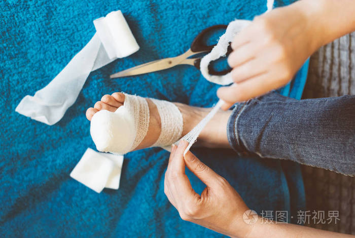 包扎她受伤的腿在家里的沙发上的女人