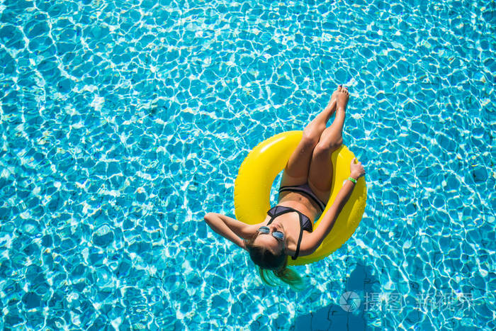 年轻漂亮的女人在游泳池里带黄色橡胶圈是放松