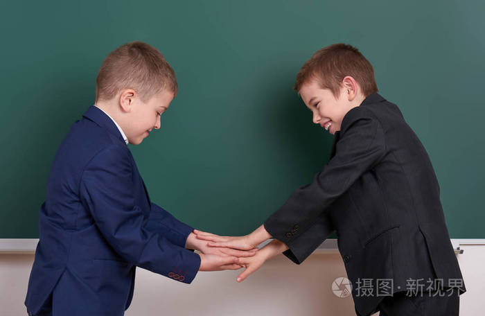 两个朋友握手,空白的黑板背景,附近的小学男孩穿着经典的黑色西装,组