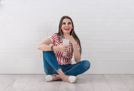 进去的意见笑快乐的年轻女子用手机和耳机, 盘腿坐着, 看着隔离的白