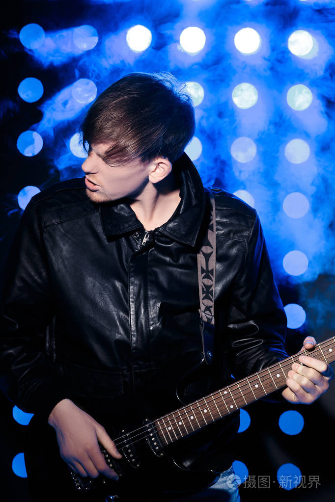 年轻的摇滚音乐家弹电吉他和唱歌.对背景的聚光灯的摇滚明星