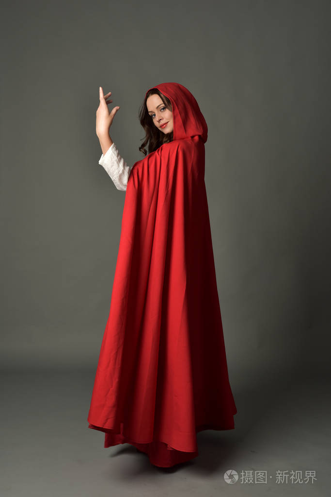 穿红色幻想服装的深色女士的全长肖像,披着斗篷,站在灰色工作室背景上