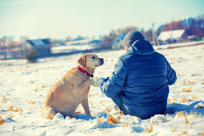 冬天,一个人和一只狗坐在村子附近的雪场上.