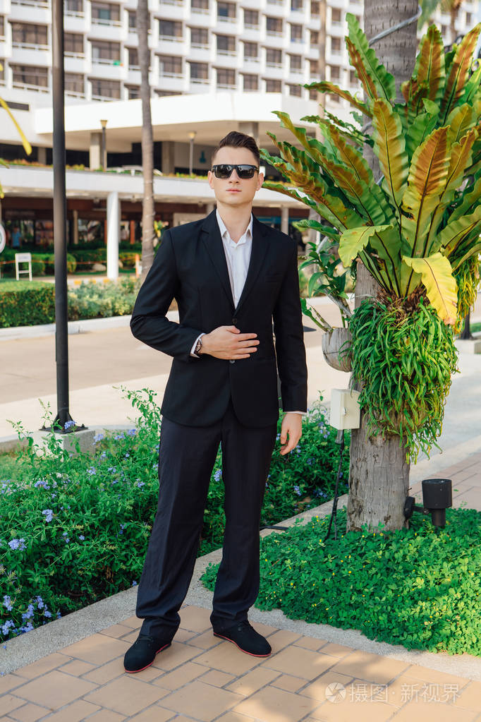 年轻时尚的帅哥在现代城市公园摆姿势,穿西装和太阳镜.