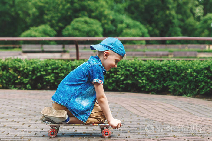 一个小城市男孩和一个滑板。一个年轻人骑在滑板上的公园里。城市风格。城里的孩子。一个孩子学会骑滑板