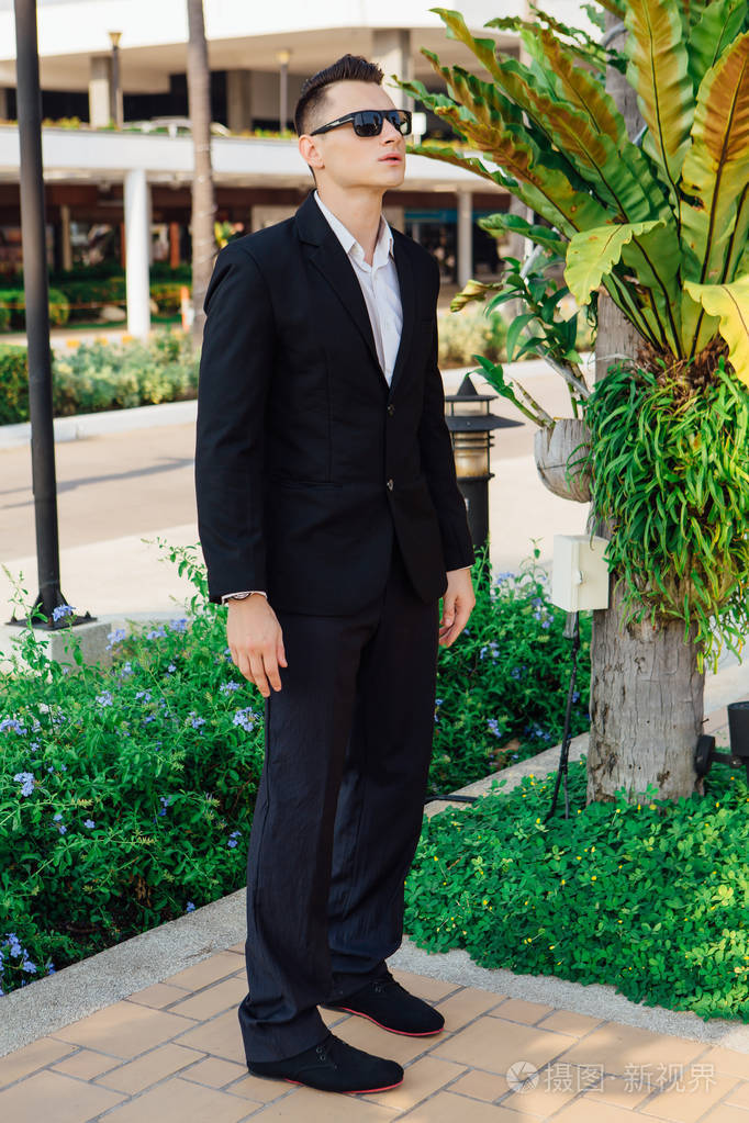 年轻时尚的帅哥在现代城市公园摆姿势穿着西装和太阳镜