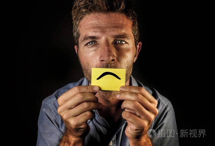 一个年轻,有魅力,沮丧的人拿着纸,带着微笑,悲伤的嘴,在他的嘴唇上画