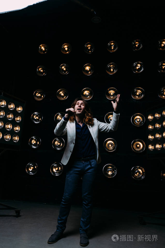 男歌手带着麦克风在舞台上留着长发,背景是明亮的灯笼场景