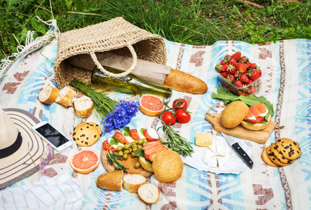 草莓番茄沙拉野餐设置在草地上,有篮子三明治,水果,草莓沙拉和橄榄.
