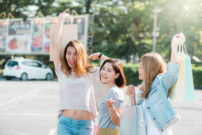 一群年轻的亚洲女人在户外市场购物，手里拿着购物袋。 年轻女性在温暖的阳光下展示她们在购物袋里得到的东西。 团体户外购物理念。