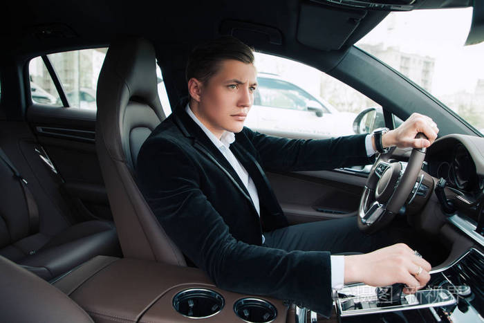 侧面视图肖像的英俊残酷严肃的年轻商人坐在车里, 开车到他的巨大的