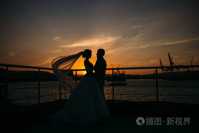 新娘和新郎的剪影站立在夜城市背景和温柔地看彼此在日落爱和家庭的