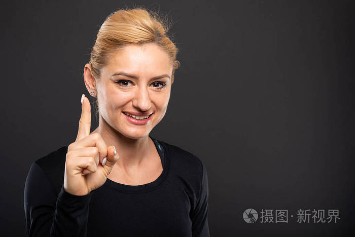 漂亮的健身房女教练的肖像,在黑色背景上显示第一个手势,带有复制广告