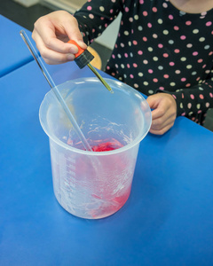 科学家的女孩女孩用液滴将黄色添加到红色diy手凝胶底座中进行颜色