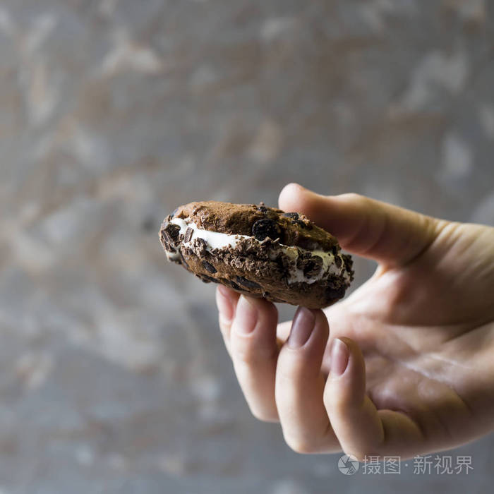 一只雌性手拿着一个冰淇淋三明治,灰色背景上有一块巧克力饼干. 夏季