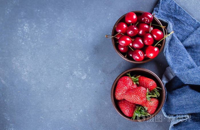 夏季草莓和樱桃在蓝色混凝土桌子上的木盘背景健康食品概念