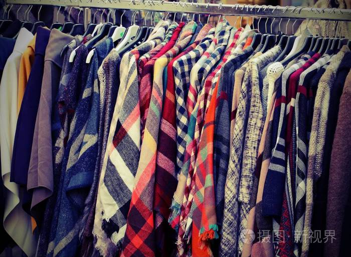 许多旧衣服挂在跳蚤市场的摊位上,许多其他旧衣服