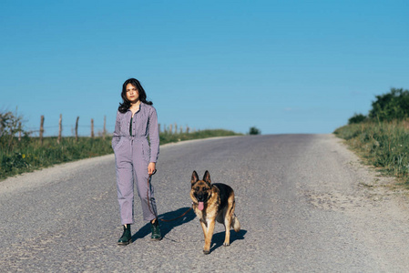 一个漂亮的女孩在路上牵着一只狗在她旁边.照片
