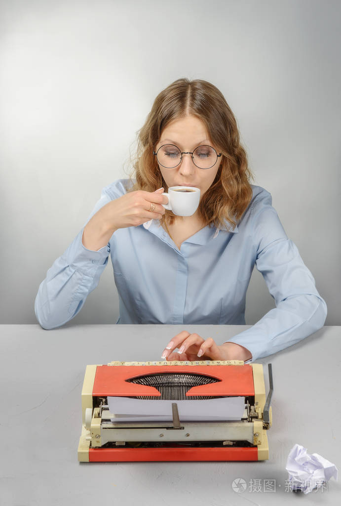 秘书戴着眼镜，用打字机在灰色背景上喝咖啡。