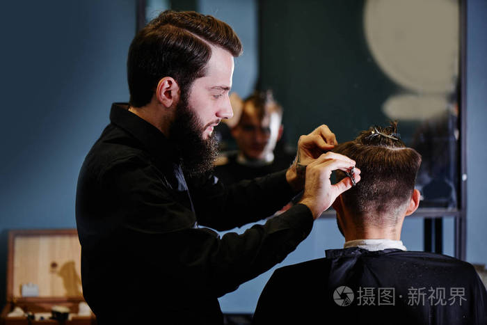 理发师穿着黑色衬衫在理发店剪一个顾客的过程中