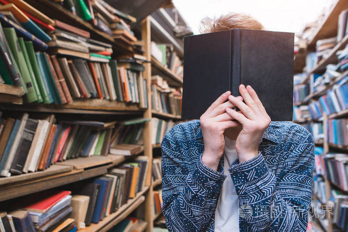 学生站在一个舒适的旧的公共公告并把书在他面前那个年轻人用脸把书合