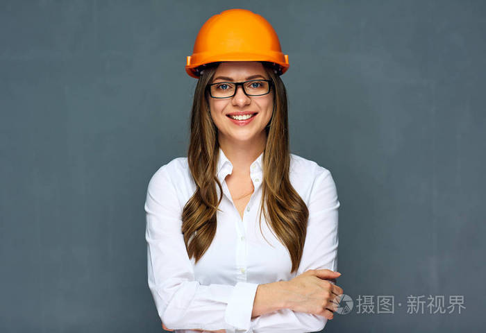 微笑的女工程师戴着建筑工人的头盔和白衬衫,交叉双臂站立着