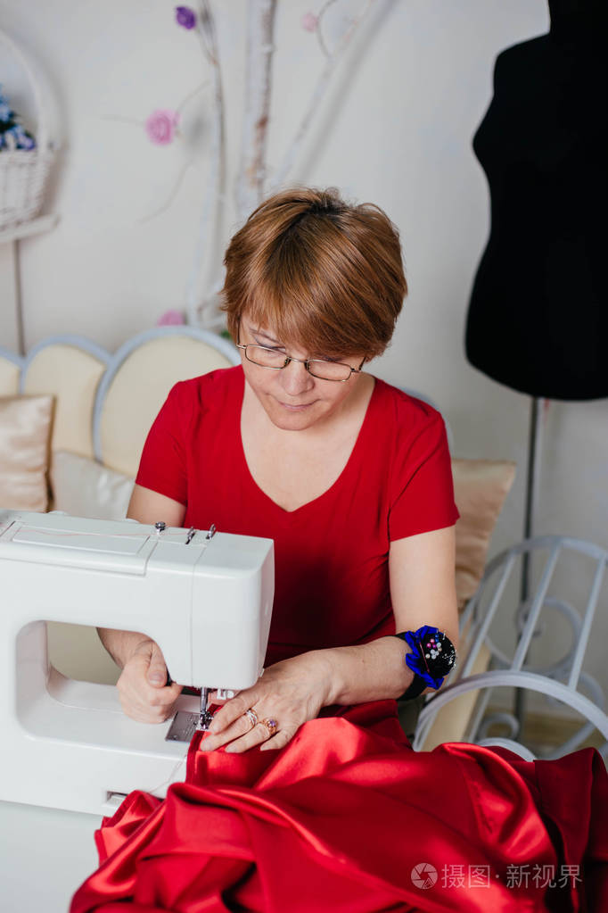 穿红色衣服的女裁缝在缝纫机上缝纫. 更好的裁剪过程.