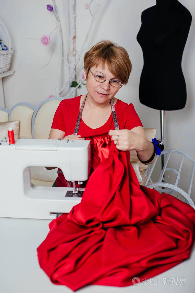穿红色衣服的女裁缝在缝纫机上缝纫更好的裁剪过程