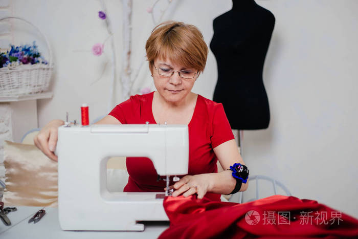 穿红色衣服的女裁缝在缝纫机上缝纫更好的裁剪过程