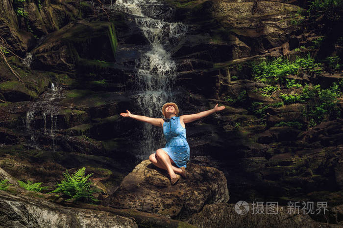 戴帽子的女人在森林瀑布附近享受大自然。 放松和自由的感觉。