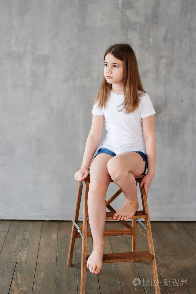 白色t恤小女孩坐在灰色背景的木椅上的肖像