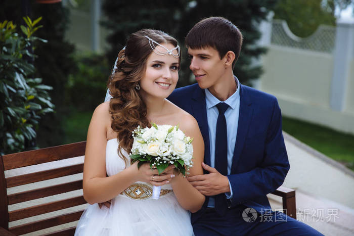 新娘和新郎的肖像他们愉快地微笑着拥抱着坐在公园里男人温柔地拥抱他