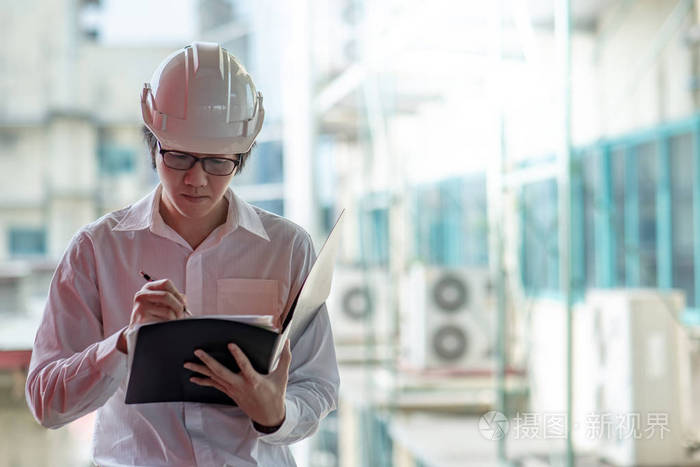 年轻的亚洲工程师或建筑师在施工现场戴个人防护设备安全帽时持有档案