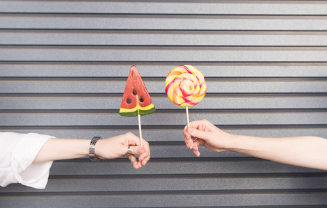 两个微笑的时尚女朋友手里拿着糖果背景是灰色的墙壁两个穿着时尚浅色