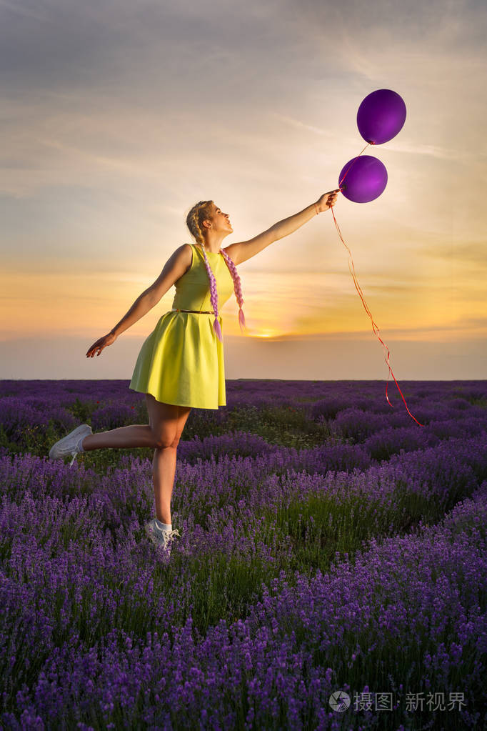 年轻漂亮的女孩穿着黄色的裙子在天空中飞翔手里拿着气球背景是薰衣草