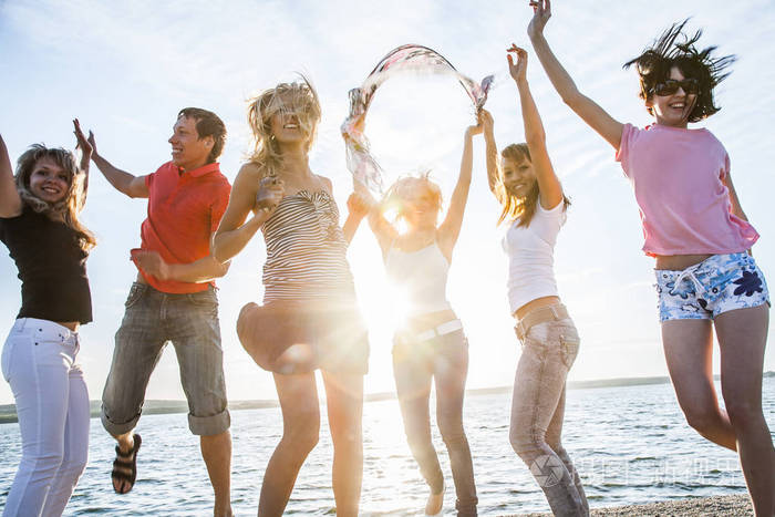 一群快乐的年轻人在美丽的夏日夕阳下在海滩上跳舞