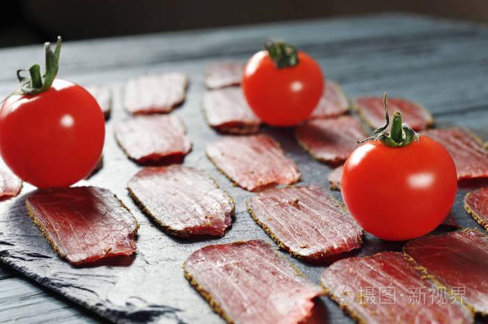 带香料的红烟熏肉片和带木蓝桌的黑板上成熟的西红柿