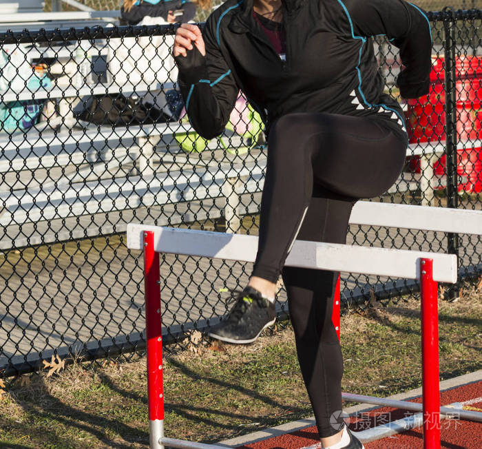 一个高中女孩正在为她的跨栏比赛热身,通过表演跨栏的练习.