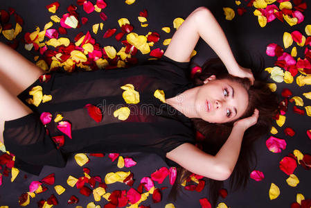 美丽的年轻女人躺在稀疏的玫瑰花瓣上