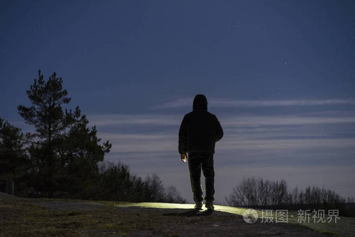 一个人站在户外的夜晚,在森林里用手电筒向前照射