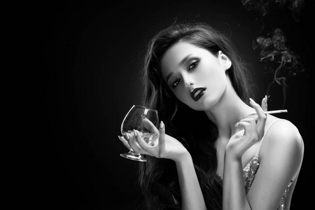 女孩穿着闪闪发光的连衣裙,在她的手中拿着一杯带冰的威士忌和一支烟
