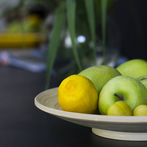 水果柠檬绿苹果黄梅放在黑木桌上的盘子里照片