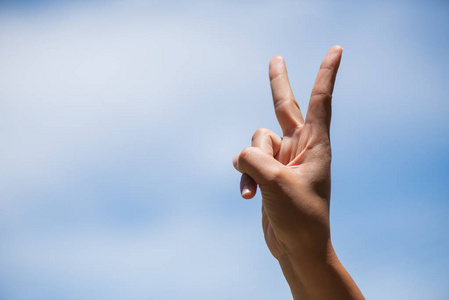 蓝天白云背景下的女子手,用两根手指作为胜利标志照片