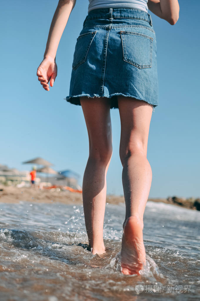 一个年轻的女孩赤脚跑在海边沙滩上从后面的底部视图