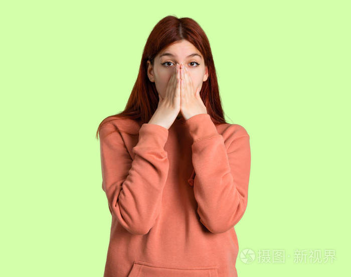 年轻的红头发女孩,穿着粉红色的运动衫,用双手捂住嘴,因为她说了一些