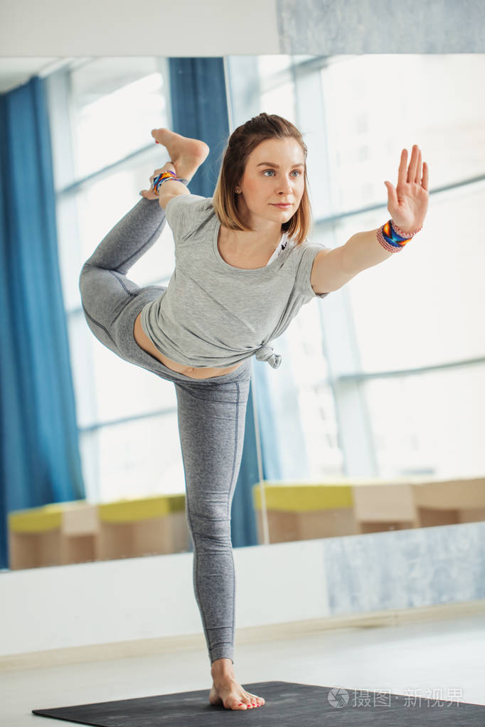 年轻的健身妇女做瑜伽姿势站在一条腿上升