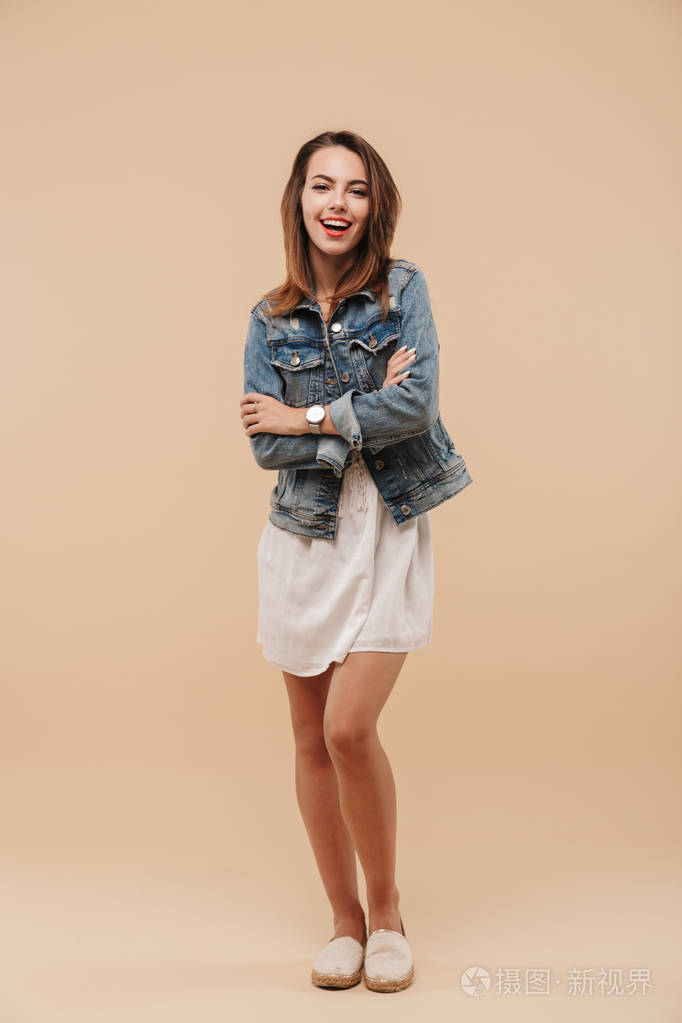 一个穿着夏装,双臂交叉,米色背景的微笑少女的全身画像照片-正版商用