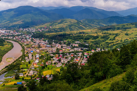 农村条小河在一个小河道旁的一条宽阔的绿色山脉脚下的农村聚落照片