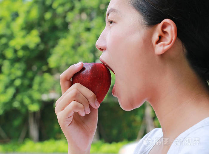 特写年轻的亚洲女孩在花园里吃苹果